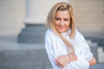 Fototapeta premium portrait of a blonde on a building background with columns. beautiful blonde in a white blouse smiling