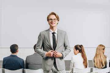 cheerful handsome coach looking at camera during business training in hub