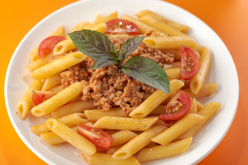 Pasta Fettuccine Bolognese with tomato sauce and basil in white dish on the orange background.