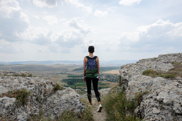 Obraz premium young woman standing on top of a hill and looking forward to the plain. Female hiker on top of mountain enjoying view. Travel, freedom, vacation, trekking, hiking concept