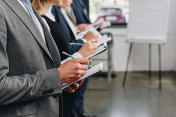 cropped image of businesspeople standing in row and writing something to notebooks during training in hub