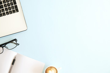 Minimalistic flat lay composition of black & white laptop computer keyboard, cup of coffee & folded glasses, blank pages notebook, pen, blue desk table background. Workspace top view, copy space