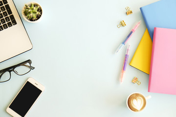 Office workplace with laptop, multiple colorful notebooks, blank screen mobile cell phone, white cup of coffee, supplies and stationery on blue background. Close up, copy space, top view, flat lay.