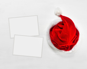 Bright red Santa Claus hat with paper frames for text or photos on wooden background.