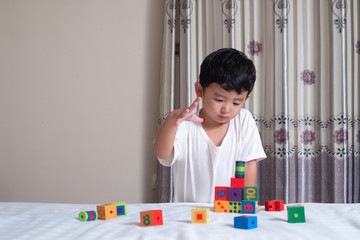 3 years old little cute Asian boy play toy or square block puzzle at home on the bed, kid lying learn by playing block shape or pieces, education and healthy concept idea.