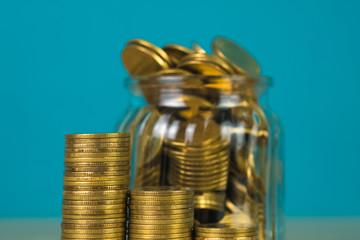 Coins stacks and gold coin money in the glass jar on table with green background, for saving for the future banking finance concept.