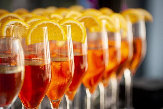 Beautiful line of different coloured cocktails, tequila, martini, vodka, and others on decorated catering bouquet table on open air corporate or wedding party