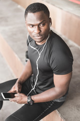 Fototapeta na wymiar Young male jogger athlete training and doing workout outdoors in city. a black man resting after a workout and listening to music and watching a sports watch