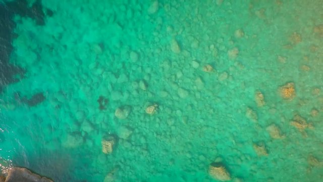 Aerial view of turquoise water with stones in the background on an beach.