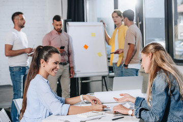 Obraz premium smiling businesswomen looking at documents during meeting in office