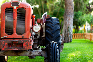 An old vintage red tractor near a farm field at sunset