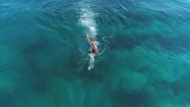 Aerial shot of young man swims at sea.