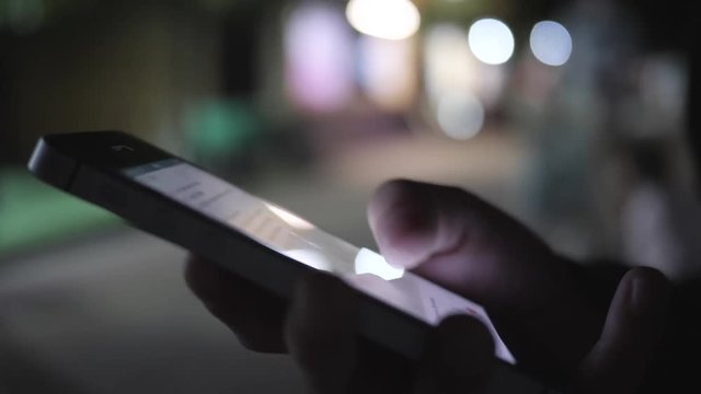 Close-up image of a child's hands using a smartphone at night on a city shopping street, search or social network concept, a hipster man typing a sms message to his friends