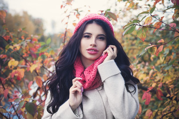 Beautiful autumn woman with long dark hair holding red maple leaf outdoors. Beautiful girl in fall park
