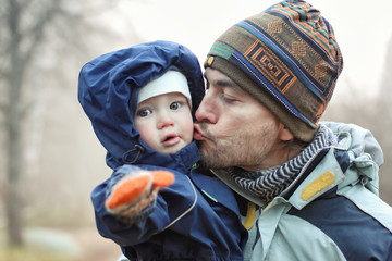 Father kises his toddler son outdoor. Cold weather, autumn or winter