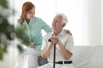 Friendly nurse and smiling elderly man with walking stick in the nursing house