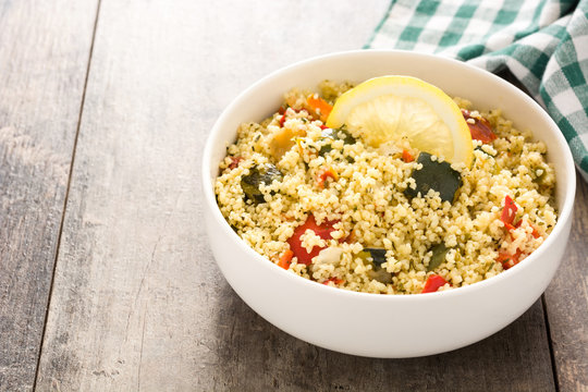 Couscous with vegetables in bowl on wooden table. Copyspace