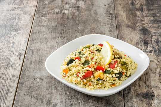 Couscous with vegetables in plate on wooden table. Copyspace