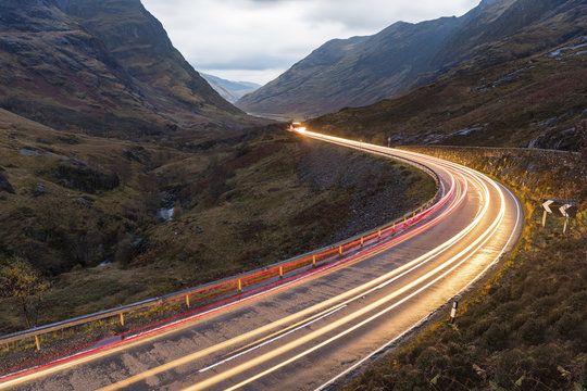 UK, Scotland, car light trails on scenic road through the mountains in the Scottish highlands near Glencoe at dusk