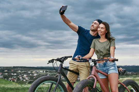 Happy couple with fatbikes taking selfie by smartphone outdoors