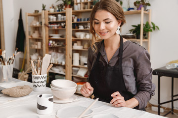 Young female ceramist working by hands in pottery studio.