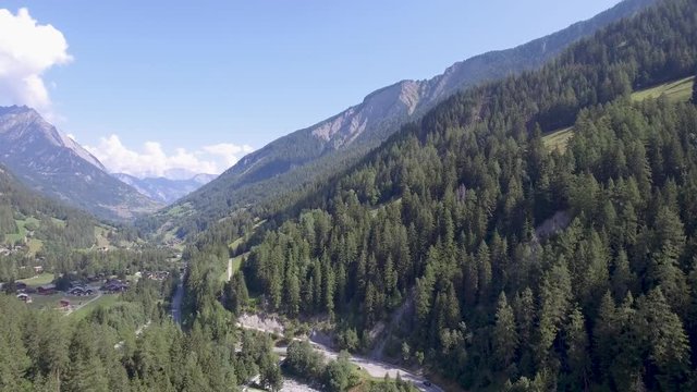 Stunning Drone footage over a mountain  river and forest winding through a tree lined alpine valley in Switzerland. A road boarders the river and passes through the trees down into the distance.