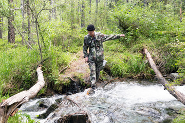 A man crosses a log through a mountain stream. A tourist walks along a makeshift bridge across a cold mountain river.