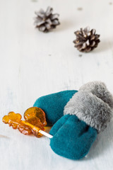 
  Warm children's mittens with fur trim, candy lollipop and pine cones on a light wooden background.