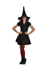 full length portrait of red haired girl wearing black witch costume and pointy hat.  standing pose, isolated on white studio background.