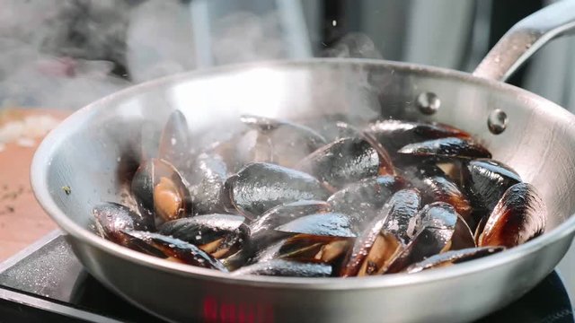 Chef salting mussels on hissing frying pan.