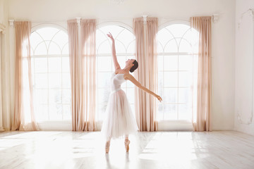 Ballerina dancing in a studio on white background window.