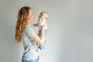 Young mother holding her newborn child. Woman and infant boy relax and playing on white background. Mom of breast feeding baby. Family, maternity, tenderness, parenthood, responsibility concept