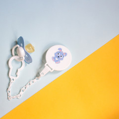 baby blue pacifier with a pin on a colored yellow and blue background, copy space