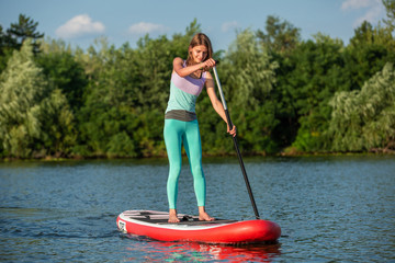 Woman is floating on a SUP board on sunny morning. Stand up paddle boarding - awesome active recreation during vacation.
