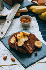 Chocolate banana bread on a black slate, with bananas and nuts for breakfast.