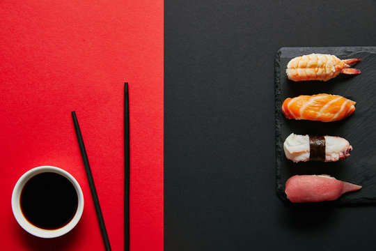 flat lay with soya sauce in bowl, chopsticks and nigiri sushi set on black slate plate on red and black background