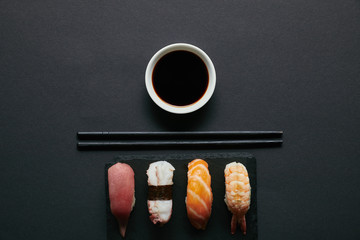 top view of assorted nigiri sushi set, chopsticks and soya sauce on black slate plate on dark tabletop