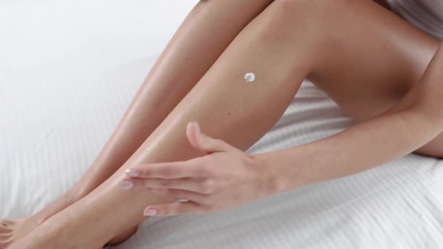 Body Care. Woman Sitting On Bed And Applying Cream On Leg Skin