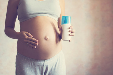 Pregnant woman pouring a cream on hand before applying on her belly.