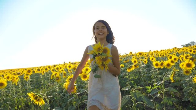 Happy little girl running happy free across the field with sunflowers. slow motion video. smelling big sunflower on summer field. Delight of a pleasant smell. Summer holiday. concept happiness