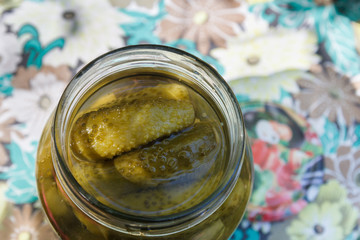 Pickles rolled in a glass jar stand on a wooden stump