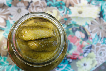 Pickles rolled in a glass jar stand on a wooden stump