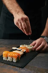 Fotobehang gedeeltelijke weergave van chef-kok die sesamzaadjes giet op gearrangeerde sushi op leisteenplaat op donker tafelblad © LIGHTFIELD STUDIOS
