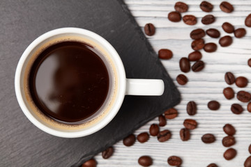 cup of coffee with coffee's beans over white wooden background, top view