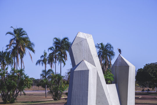 front view photo in a daylight from a square in Bras&iacute;lia with a small lake, blue sky and many concrete strutute simulating big cristals