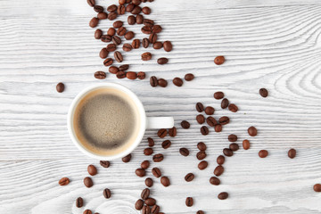 cup of coffee with coffee's beans over white wooden background, top view