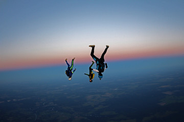 Three skydivers are falling in the evening sky.
