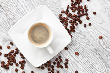 cup of coffee with coffee's beans over white wooden background, top view