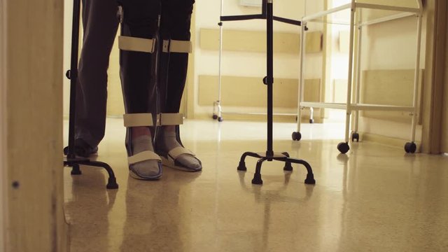 Close up legs of disable man in orthosis walking with support of two walking cane in the rehabilitation clinic. Doctor helping him.