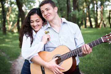 Naklejka premium young couple walking in the forest and playing guitar, summer nature, bright sunlight, shadows and green leaves, romantic feelings